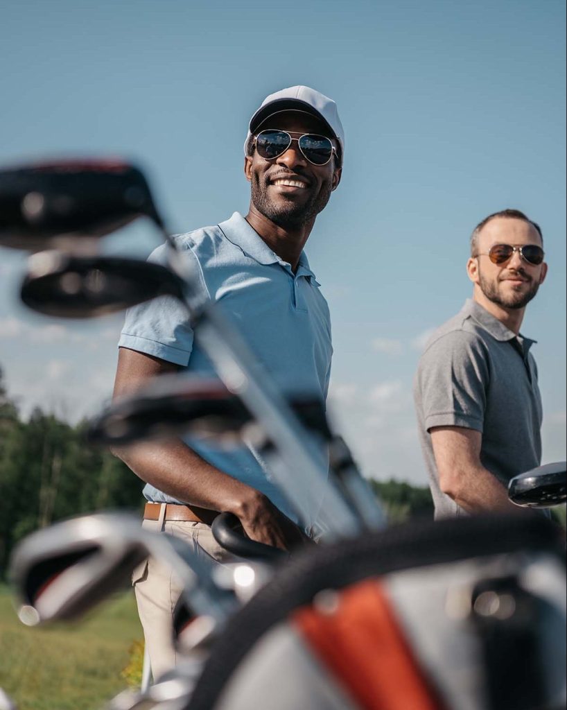 Smiling multiethnic sportsmen going to the golf co 5clzum5 e1660746767564.jpg